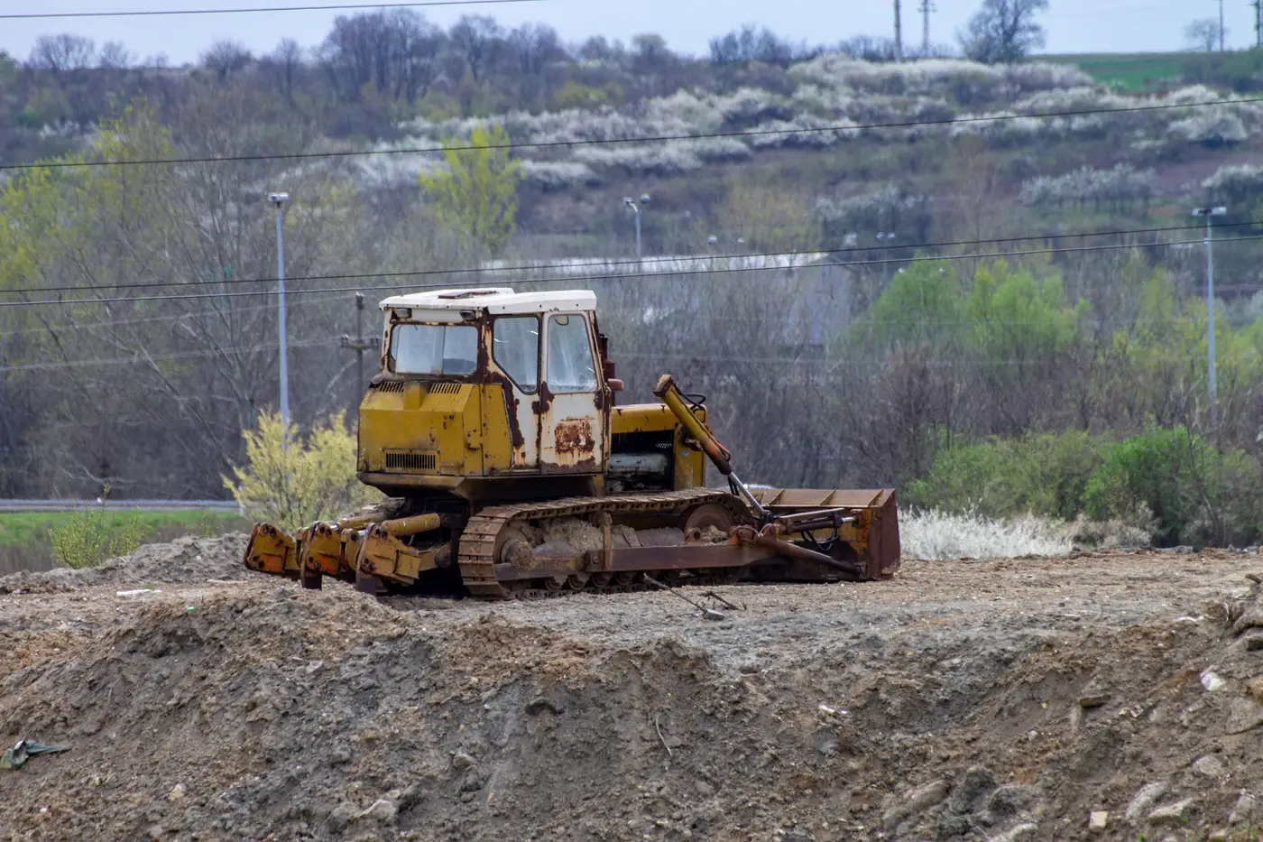 An old rusted bulldozer sitting unused in an open field, trees in the background.