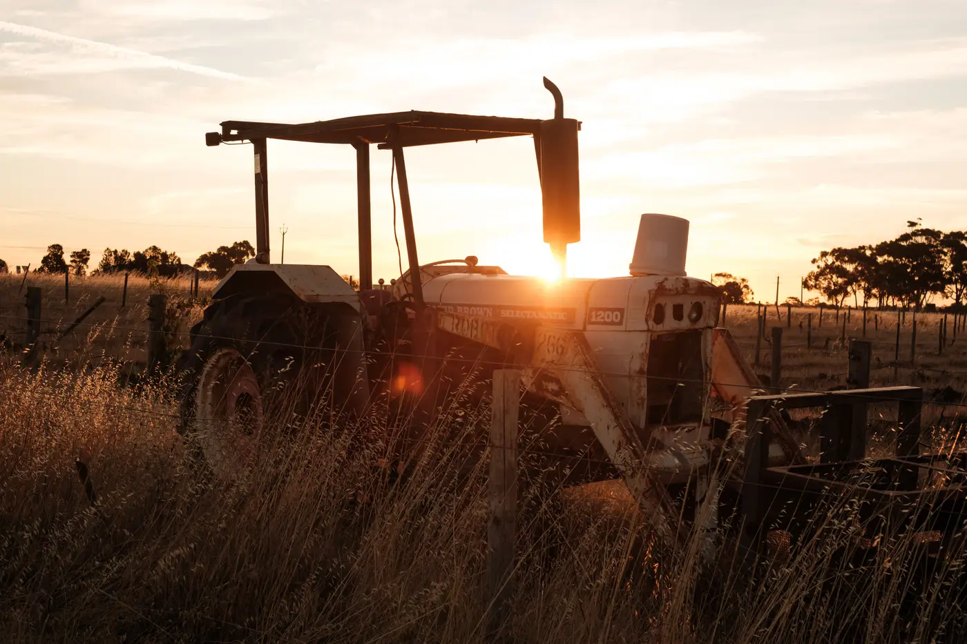 A single tractor silhouetted against a golden sunset in an open rural field.